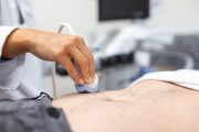 Ultrasound diagnosis of the stomach on the abdominal cavity of a man in the clinic, close-up view. The doctor runs an ultrasound sensor over the patient's male abdomen. Diagnostics of internal organs.